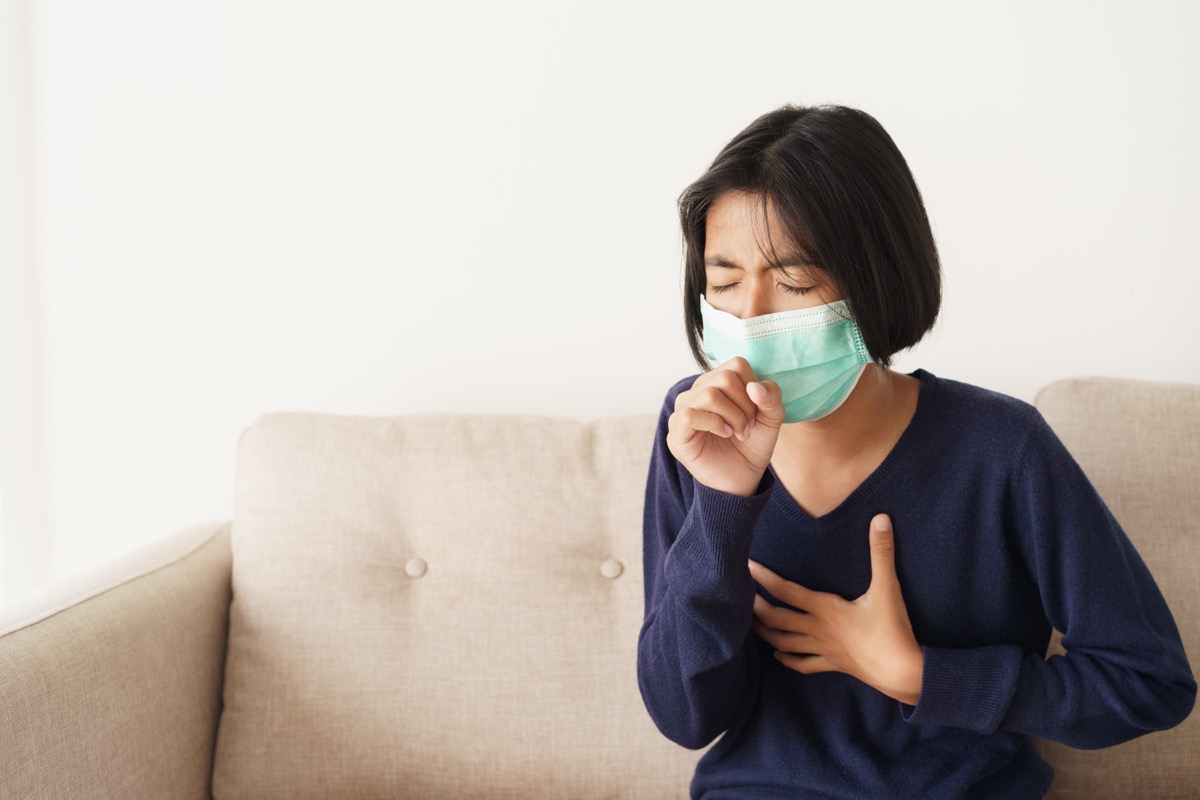 girl symptom cough and are protective with medical mask while sitting on sofa, Asia child wearing a protection mask epidemic of flu or covid-19 in living room at home. Health and illness concept