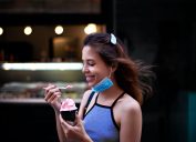 young woman eating sorbet or ice cream with coronavirus face mask