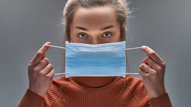 A woman holding a protective face mask over her mouth about to put it on.