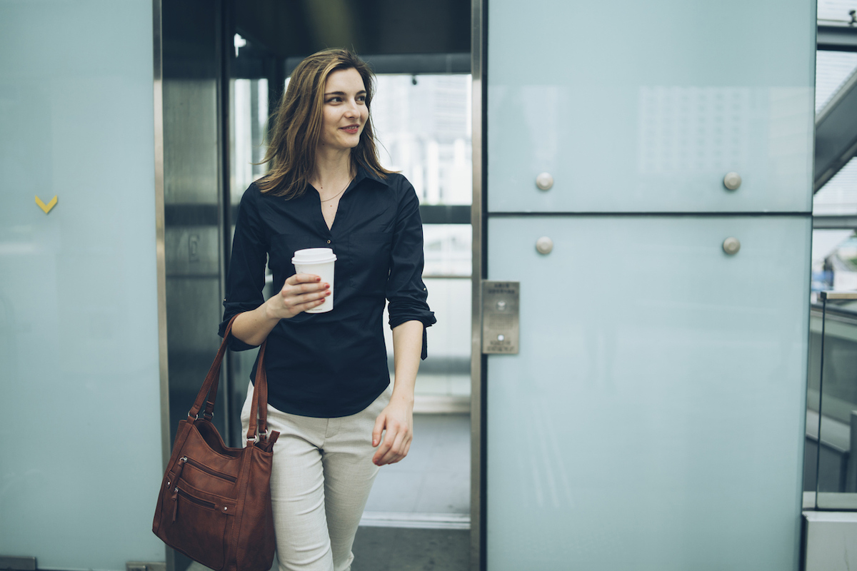 Woman leaving elevator, holding coffee cup.