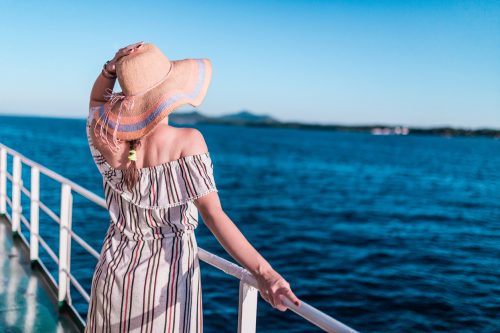 A woman wearing a hat standing on the deck of the ship and look out onto the ocean