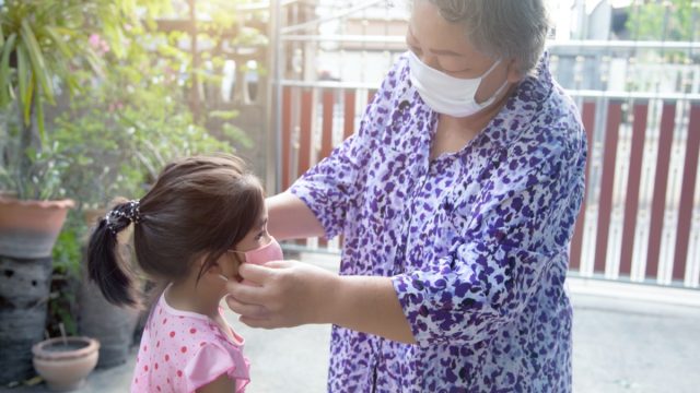 older asian woman putting mask on granddaughter