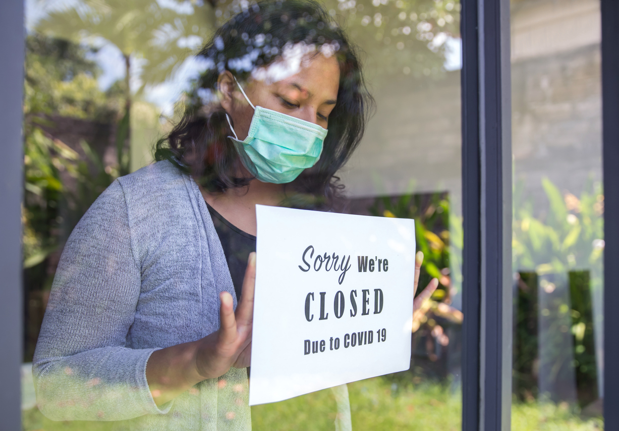 A woman wearing a face mask putting up a sign in her shop that says closed due to COVID-19