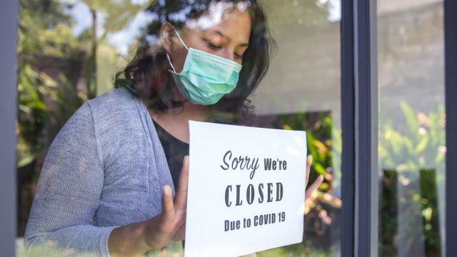 A woman wearing a face mask putting up a sign in her shop that says closed due to COVID-19
