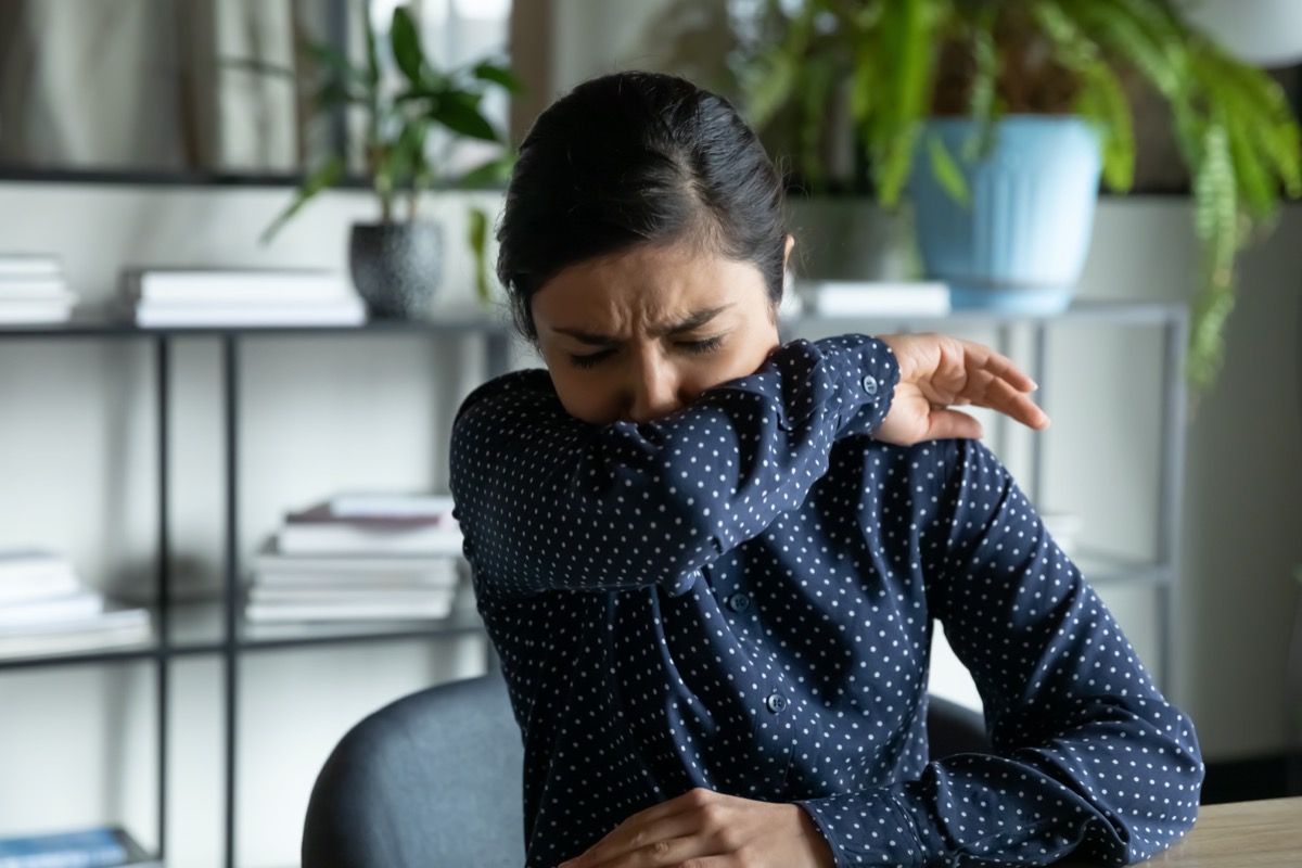 young asian woman coughing or sneezing into her elbow in an office