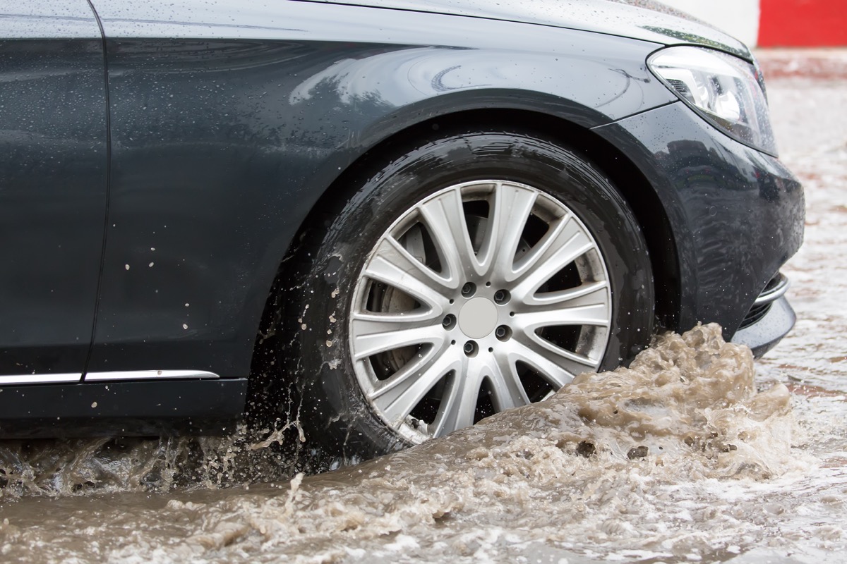 Car motion through big puddle of water splashes from the wheels on the street road