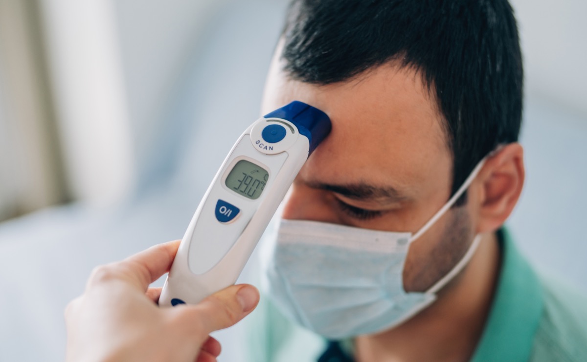 Healthcare worker checking body temperature of a young sick man with contactless digital infrared thermometer.
