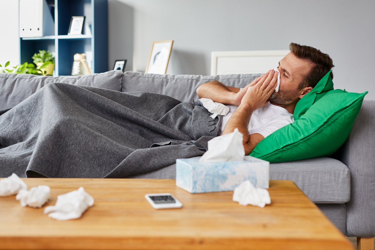 Man with a cold on the couch blowing his nose