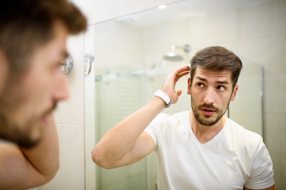Young man in the bathroom looking in the mirror and fixing his hair with dandruff
