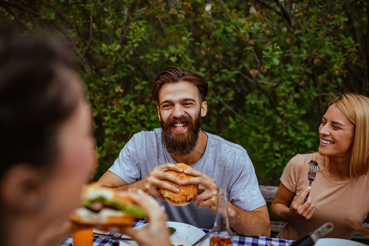 Cropped shot of a young man eating burger outdoors