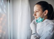 A female doctor looking out a hospital window while pulling her mask down