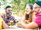 Friends drinking beer with opened face masks - New normal lifestyle concept with people having fun together talking on happy hour at brewery bar - Bright vivid filter with focus on afroamerican guy