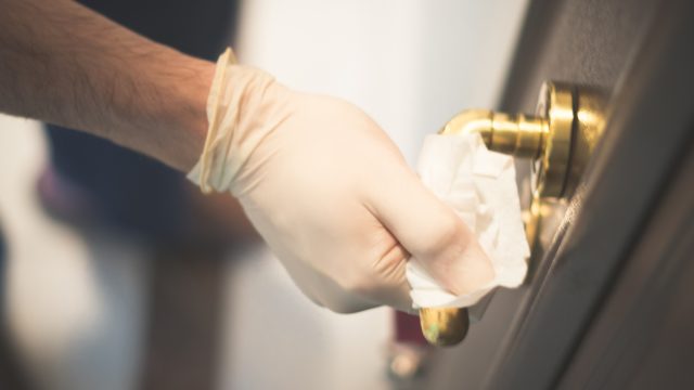 A gloves hand wiping down a doorknob with a sanitizing wipe to get rid of coronavirus