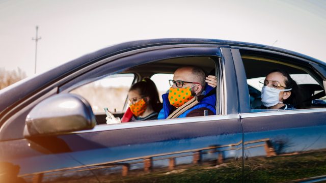 A group of young adults wearing face masks take a ride in a car with the windows rolled down