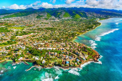 The suburban residential districts of Honolulu, Hawaii along the coastline just outside of downtown from about 1000 feet over the Pacific Ocean.