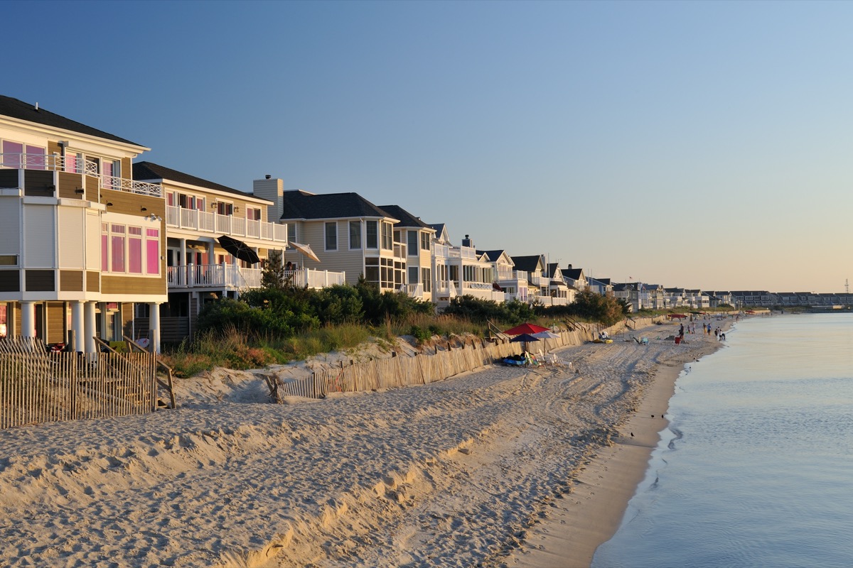 Pristine beach and luxury villa houses with people enjoying beach activities in the background on the Cape Henlopen of Delaware, where thousands of visitors come to enjoy ocean swimming and sunbathing during summertime.