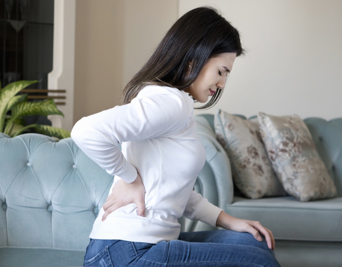 Woman with back pain holding back sitting on couch
