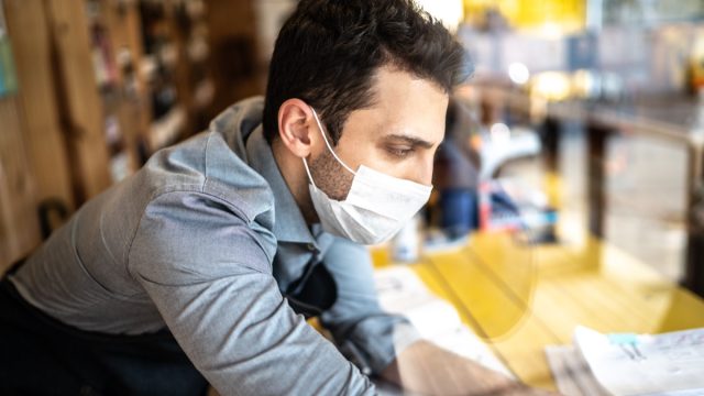 Young small business man owner with face mask working on checkout