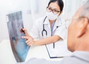 Portrait of woman doctor wear protection face mask show patient some information on digital tablet clip board, patient listen to specialist doctor in clinic office. Epidemic flu or Coronavirus.