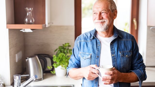Older man in kitchen drinking coffee smiling