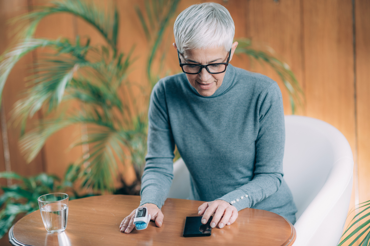 senior woman sitting at a table using a Pulse Oximeter to monitor Blood Oxygen Saturation levels