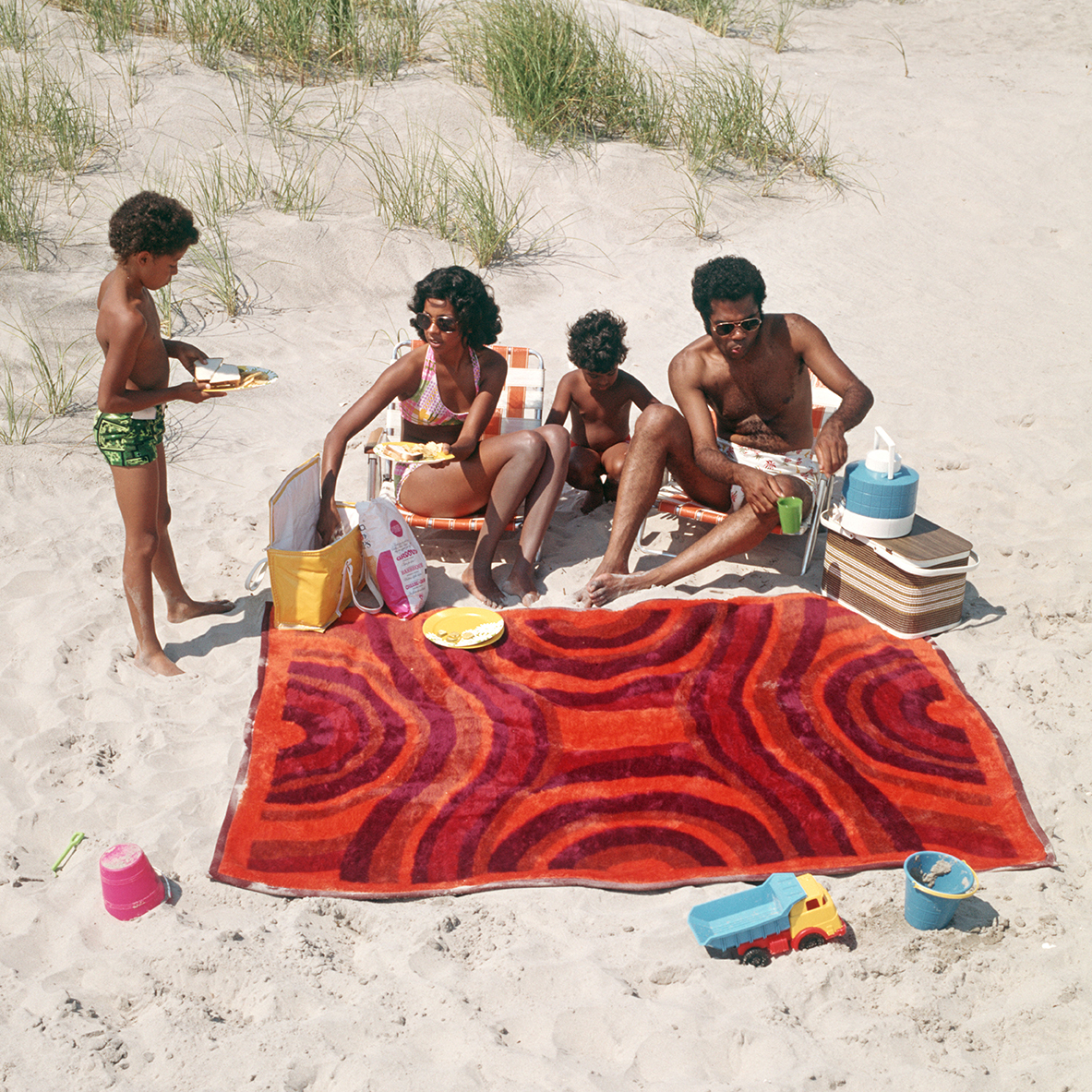 a family of four have a picnic on the beach in the 1970s