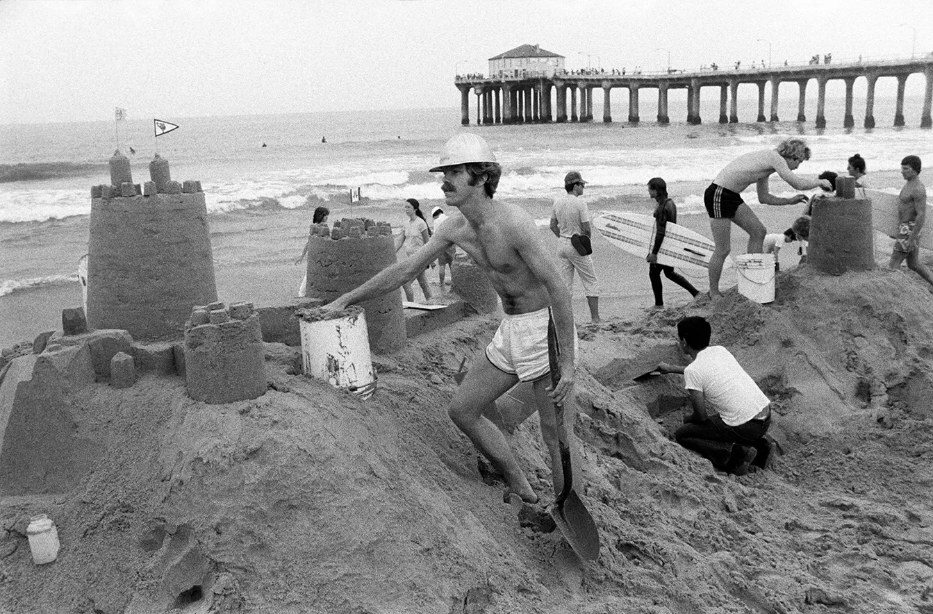 a man builds a sandcastle by a pier