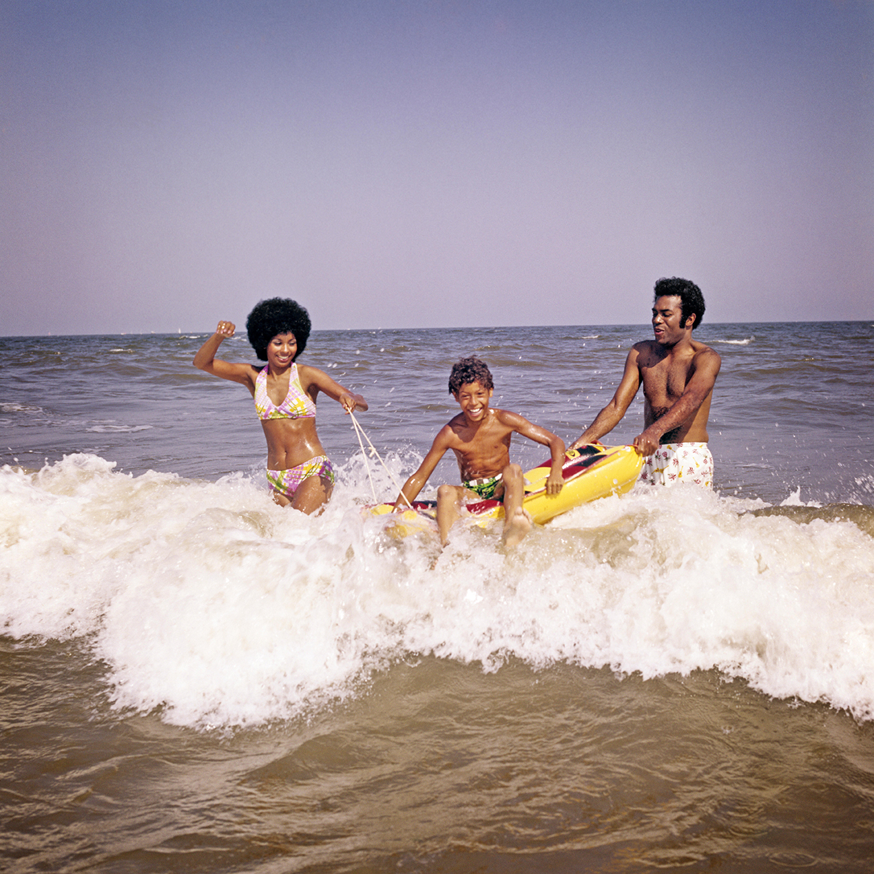 a mom, dad, and son play on a raft in the waves