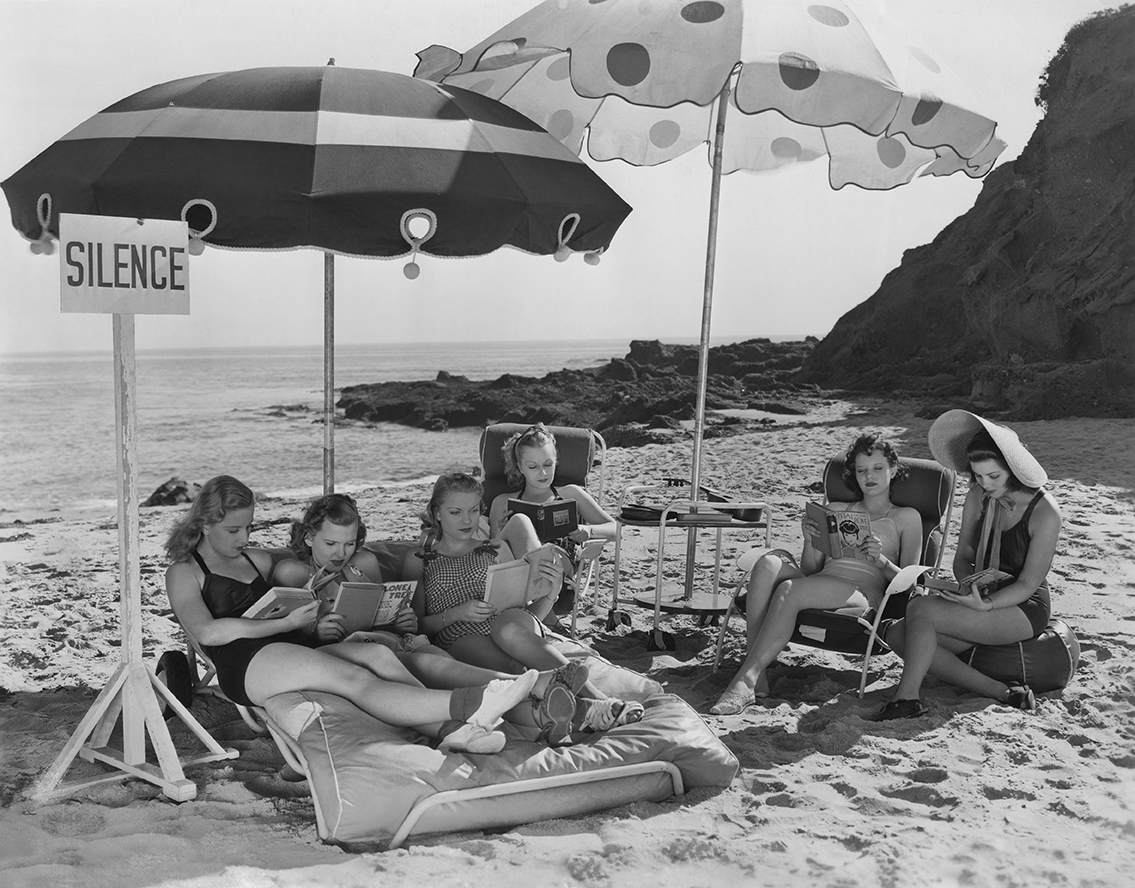 a group of women read books on the beach