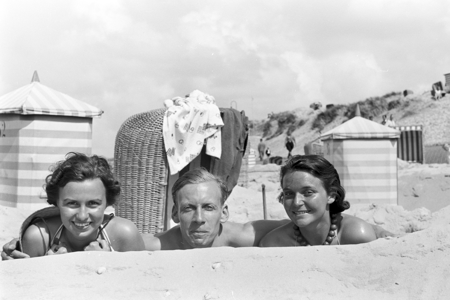 two women and a man lay in the sand at the beach