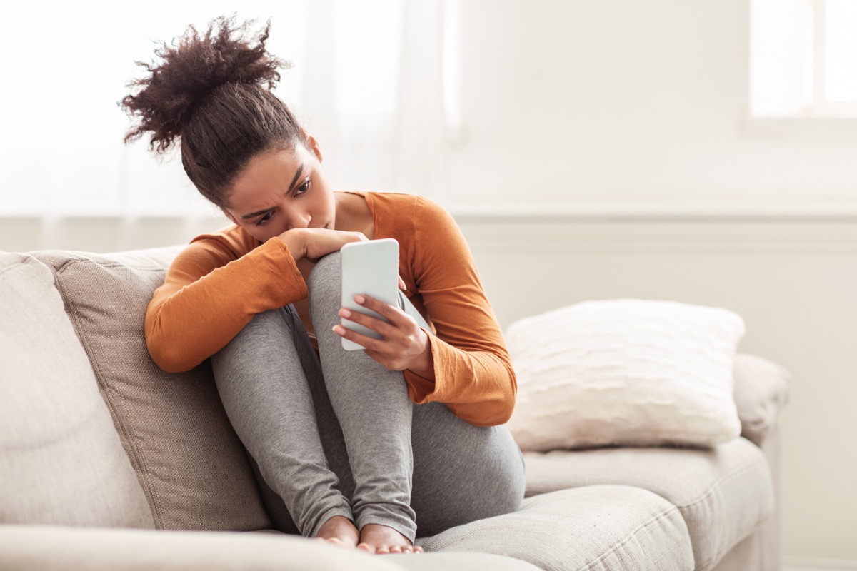 Sad woman looking at phone on couch