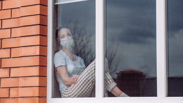 white woman with face mask sitting in a window