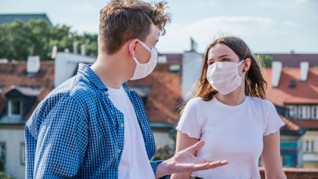 white man and white woman with face masks talking outside