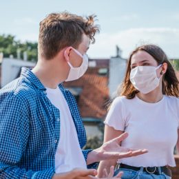 white man and white woman with face masks talking outside