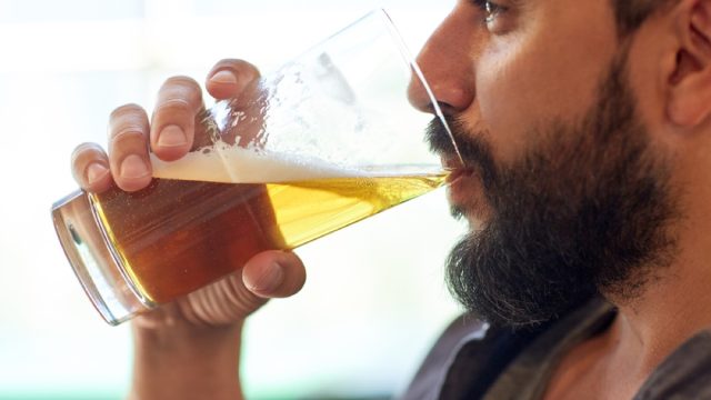 close up of bearded white man drinking a glass of beer