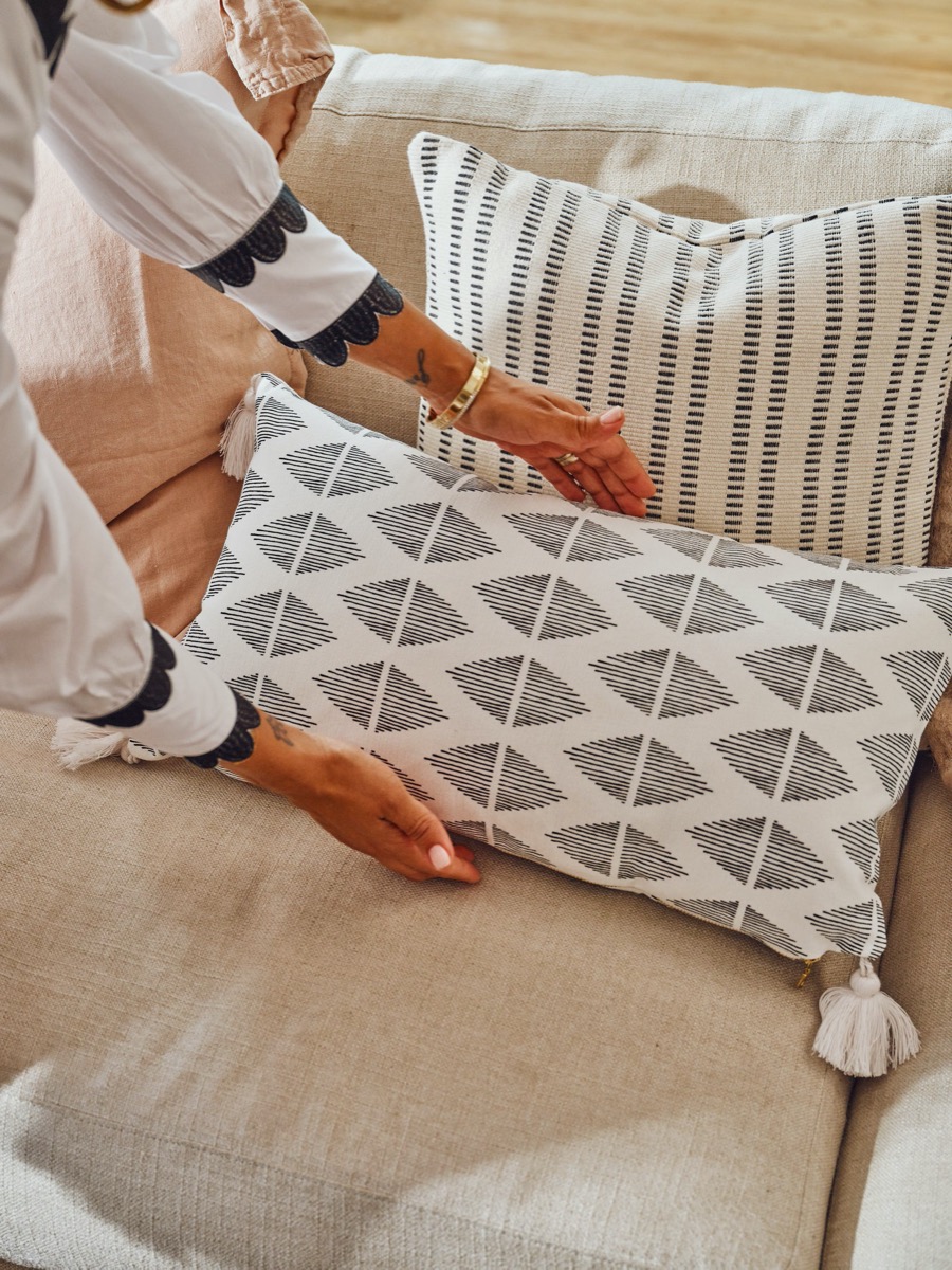 hands putting gray and white throw pillow on couch