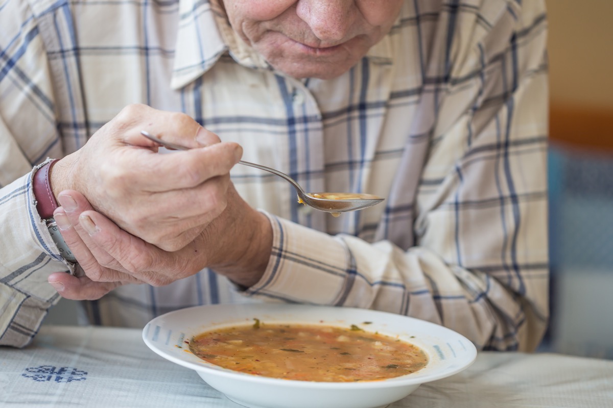 A shivering man still holding hands and eating soup