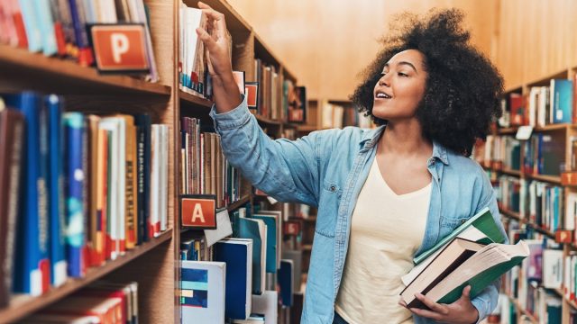 Student holding a stack of books in a library