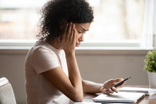 Uma jovem olha para a mensagem de texto em seu smartphone com uma expressão preocupada em seu rosto.