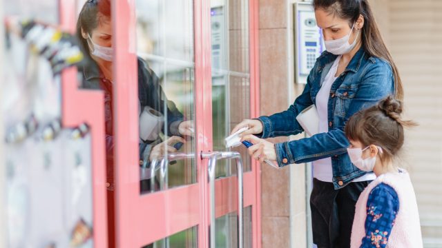 A woman wearing a face mask opens the door to a store with a napkin to prevent the spread of coronavirus while her young daughter watches