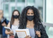 3 students of various ethnicities wearing protective face masks on their college campus.