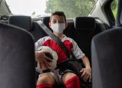Boy in a car on his way to soccer practice wearing a face mask to avoid the coronavirus pandemic