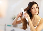 young white woman using flat iron to straighten hair