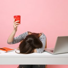 Tired woman with head on desk holding coffee