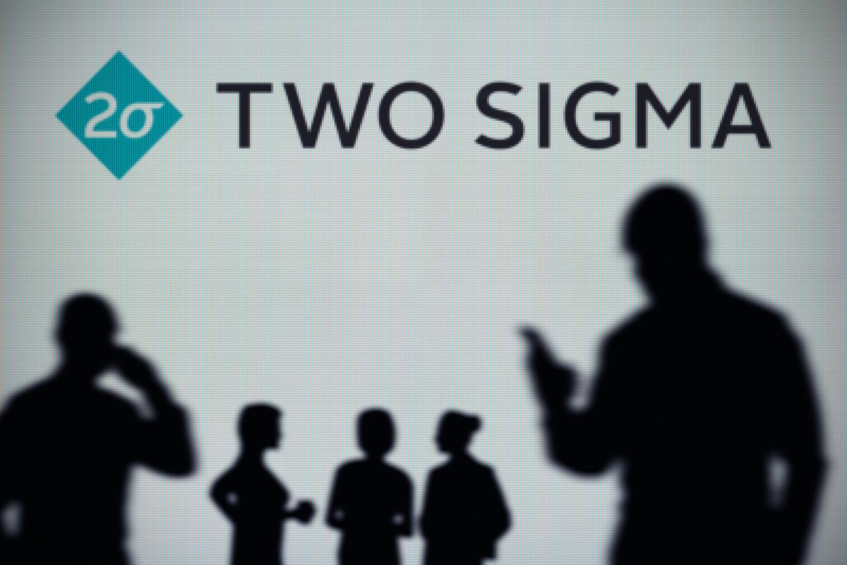 The Two Sigma logo is seen on an LED screen in the background while a silhouetted person uses a smartphone