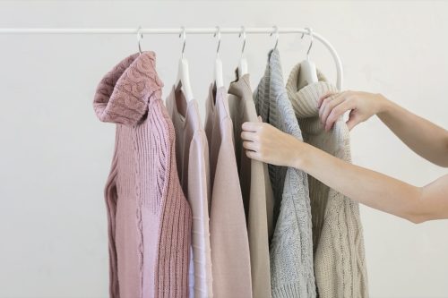 Close up on hands choosing from rack of sweaters