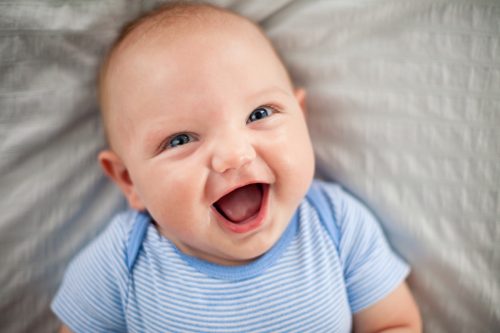 Farbenfrohes Bild eines lachenden Babys, das auf dem Rücken auf einer gemusterten Decke liegt.