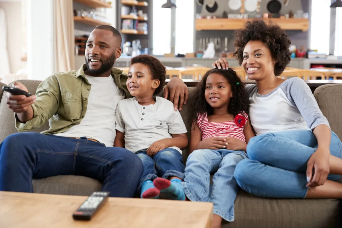 young black man, woman, and two kids sitting on couch watching TV