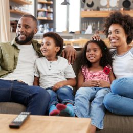 young black man, woman, and two kids sitting on couch watching TV