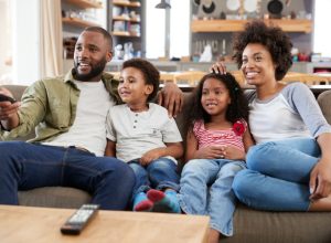 young black man, woman, and two kids sitting on couch watching TV